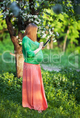 Pregnant woman using tablet PC in green park