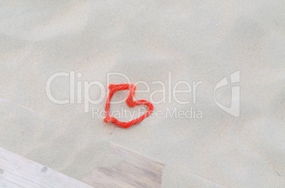 Ein rotes Seil in Herzform im Sand.
