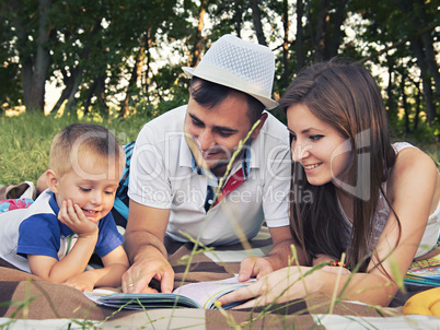 Parents with a child reading a book outdoors