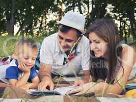 Parents with a child reading a book outdoors