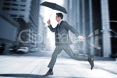 Composite image of businessman jumping holding an umbrella