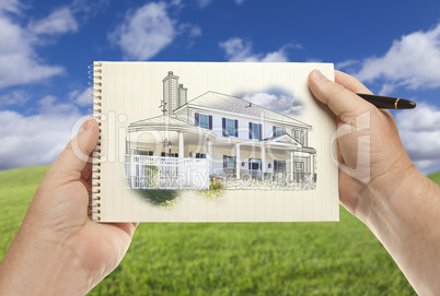 Hands Holding Paper With House Drawing Over Empty Grass Field