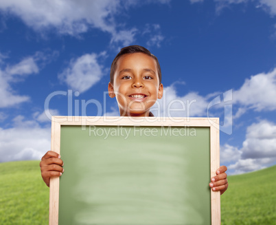 Happy Hispanic Boy In Grass Field Holding Blank Chalk Board