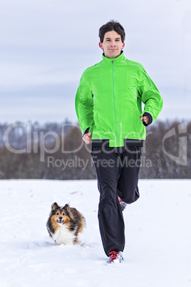 junger Mann joggt mit Hund im Schnee