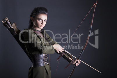 beautiful elf with bow in hand on gray background