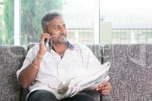 Indian man reading newspaper and calling phone