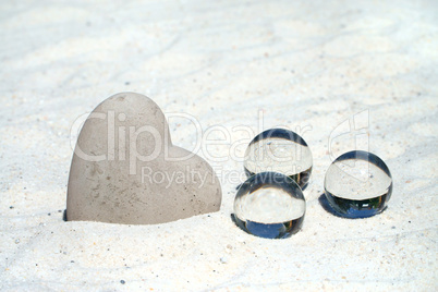 Großes Steinherz und drei Glaskugeln im Sand