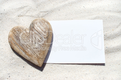 Holzherz liegt auf leerer weißer Postkarte am Strand