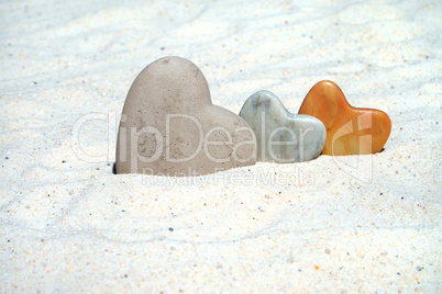Ein großes und zwei kleine Herzen aus Stein im Sand