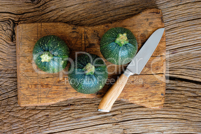Drei runde Zucchinis mit Messer auf Schneidebrett