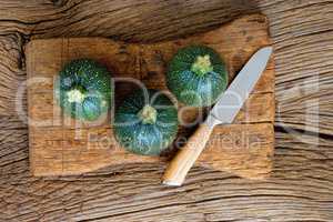 Drei runde Zucchinis mit Messer auf Schneidebrett