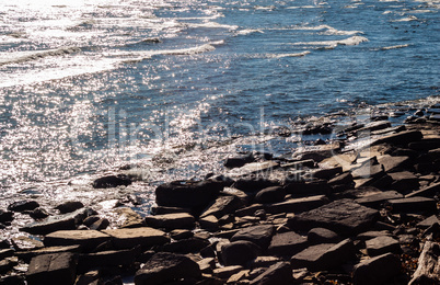 Brown rocky shore and water reflecting sunlight