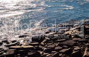 Brown rocky shore and water reflecting sunlight
