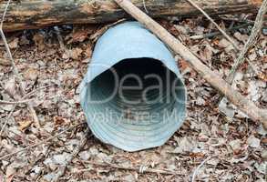 Empty metal drain pipe under log on dead leaves
