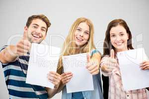 Composite image of students holding up exam and doing thumbs up