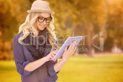 Composite image of smiling trendy blonde using tablet computer