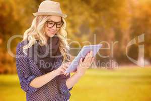 Composite image of smiling trendy blonde using tablet computer