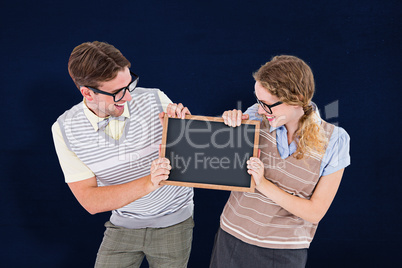 Composite image of geeky hipster couple holding little blackboar