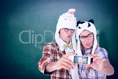 Composite image of geeky hipster couple taking selfie with smart