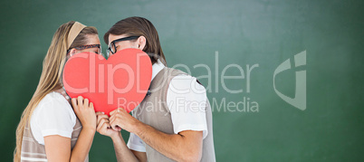 Composite image of geeky hipsters kissing behind heart card