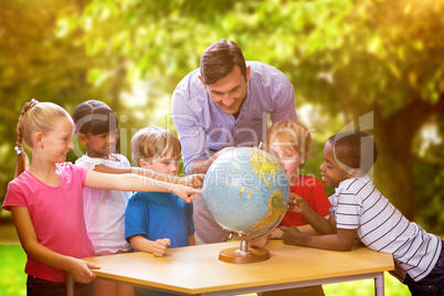 Composite image of cute pupils and teacher looking at globe in l