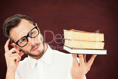 Composite image of geeky young man looking at pile of books