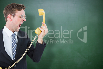 Composite image of geeky businessman shouting at telephone