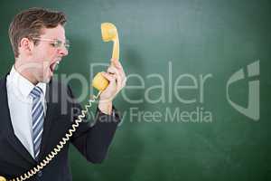 Composite image of geeky businessman shouting at telephone