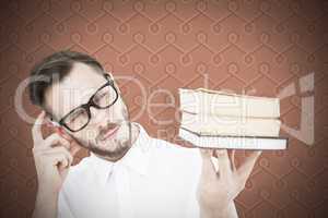 Composite image of geeky young man looking at pile of books