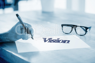 Vision  against side view of hand writing on white page on worki