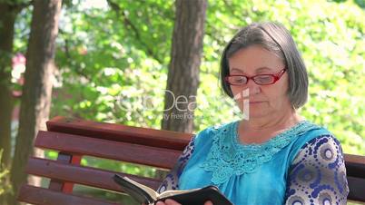 Elderly woman reading bible outdoors