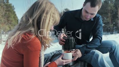 Young pair in wood. Man pours tea from a thermos.