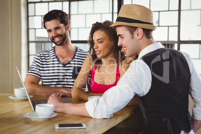 Smiling friends looking at laptop and having coffee