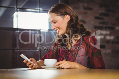 Smiling brunette having coffee and texting