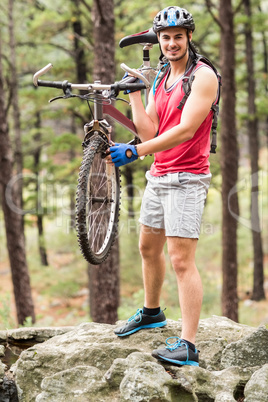 Young happy biker holding bike on a rock
