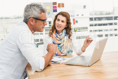 Casual designers discussing and working with laptop
