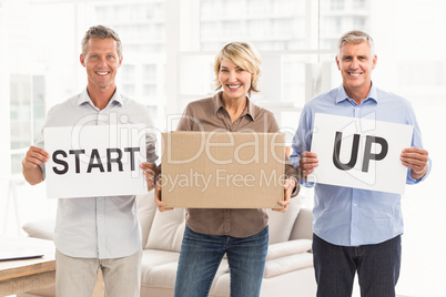 Smiling casual business people holding start up sign