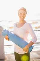 Smiling sporty woman with exercise mat