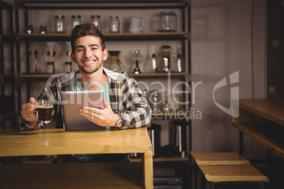 Smiling hipster having coffee and holding tablet computer