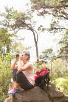 Blonde hiker sitting on rock and  looking through binoculars