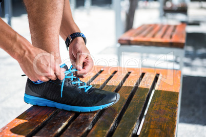 Athletic man tying his shoelaces on the bench