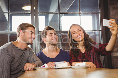 Smiling friends having coffee and taking selfies