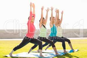 Smiling sporty women doing warrior pose in yoga class