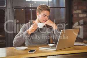 Handsome man drinking coffee and concentrating on laptop