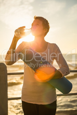 Sporty woman with exercise mat drinking water