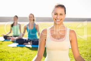 Smiling sporty brunette doing yoga with her friends