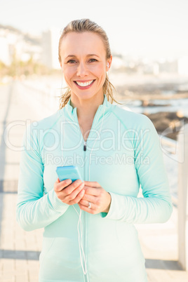 Smiling fit blonde enjoying music and holding phone