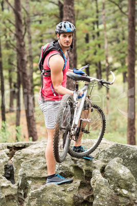 Young happy biker holding bike on a rock looking at camera