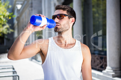 Handsome athlete with sunglasses drinking out of bottle