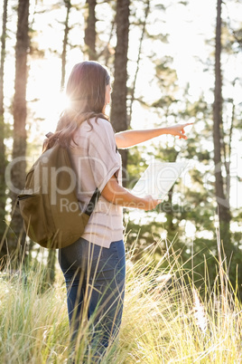 Brunette hiker with map pointing far away